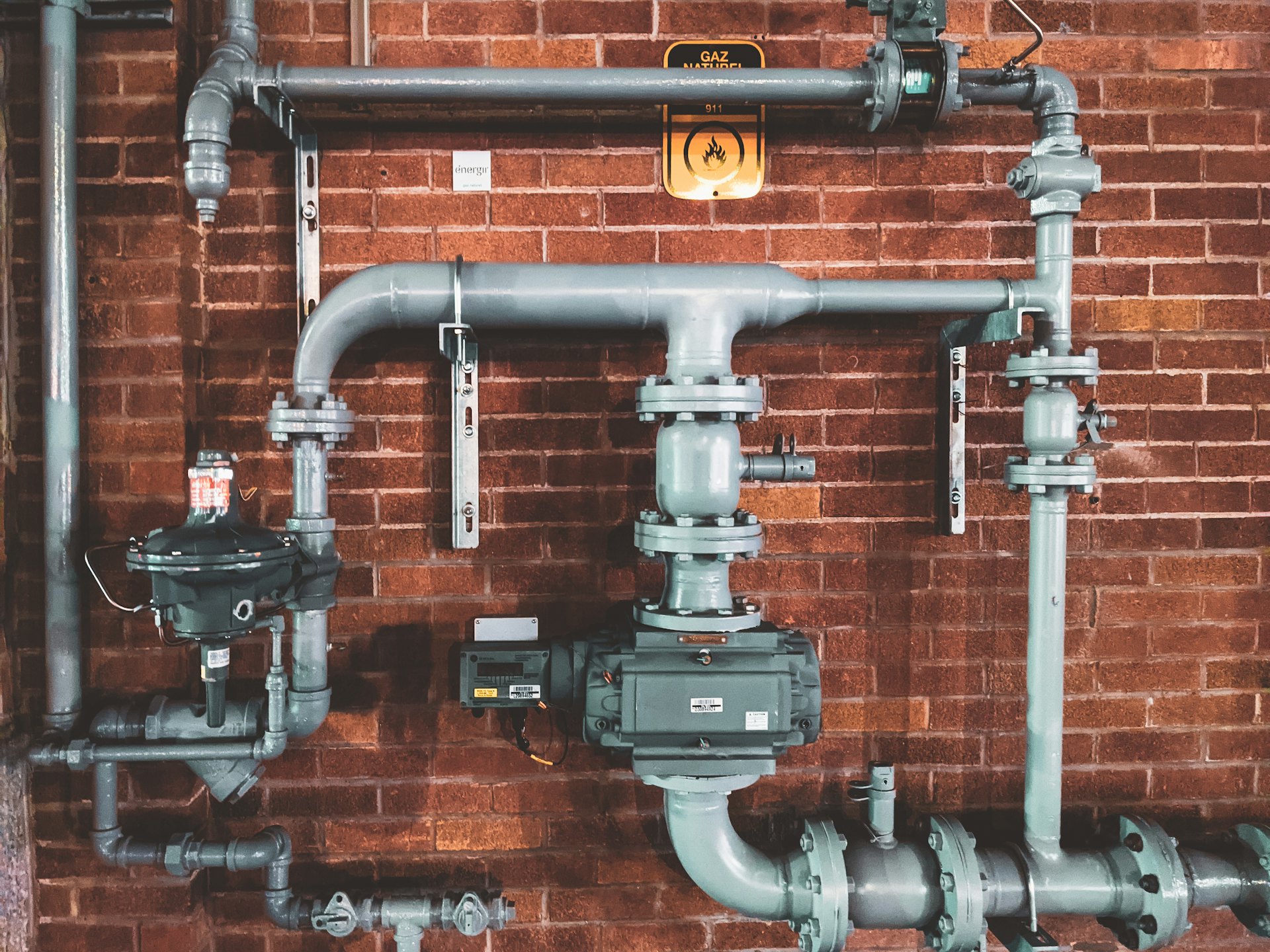 Network of industrial steel plumbing pipes mounted on a brick wall