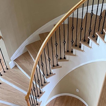 Curved oak staircase with wrought-iron balusters and a curved wood handrail, seen from above