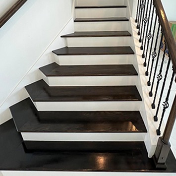 Finished dark wood stairs with a landing and wrought-iron balusters, front view