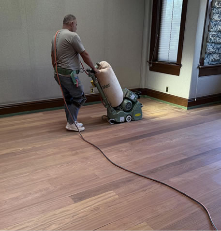 Installer sanding a hardwood floor with a drum sander in an empty room