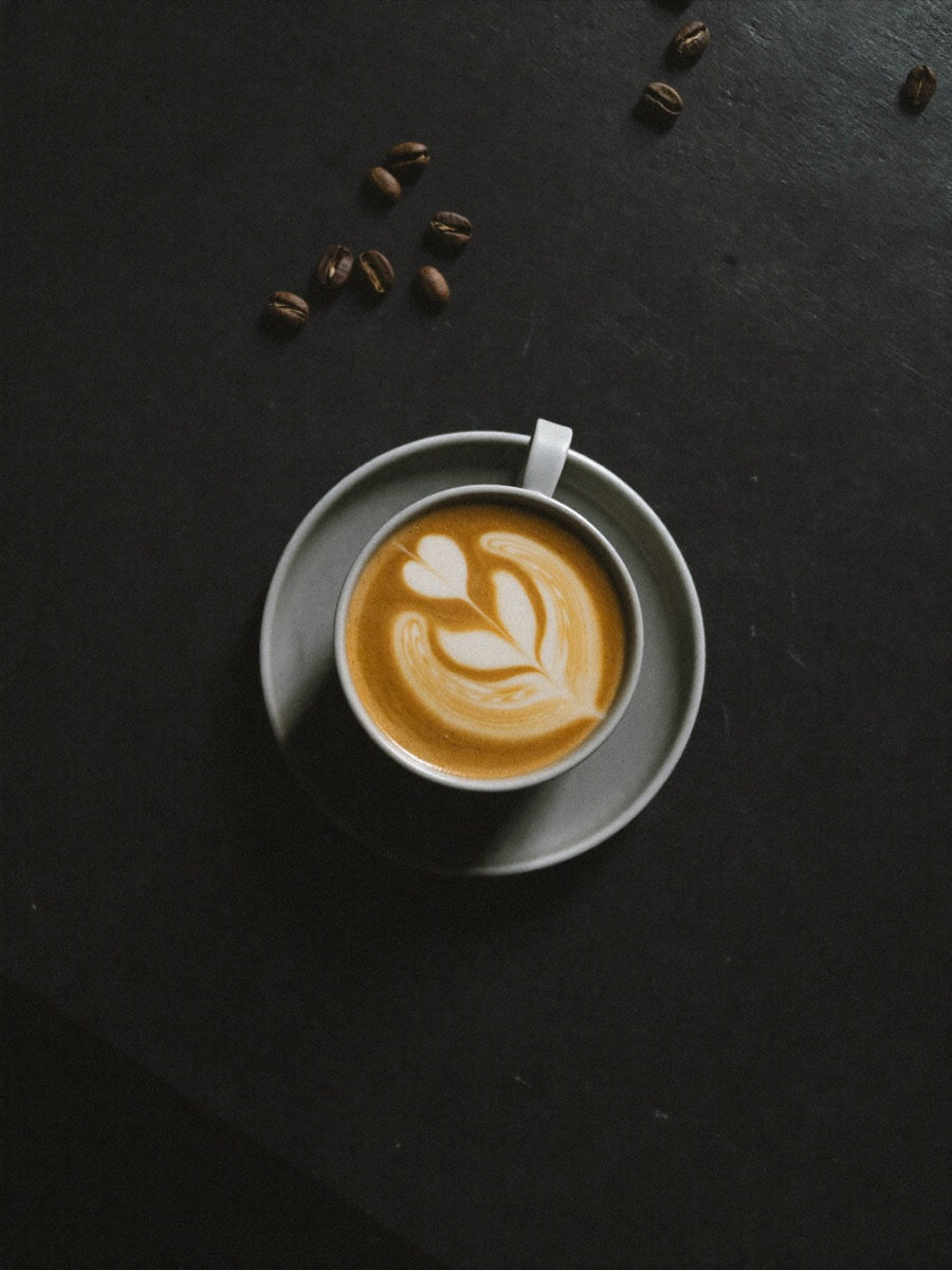 A flat white with rosetta latte art in a matte black ceramic cup on a charcoal stone table