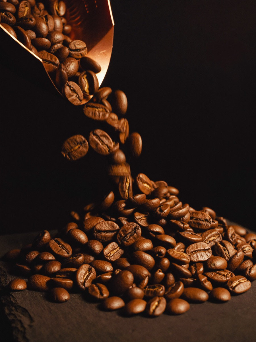Freshly roasted specialty coffee beans spilling from a copper scoop onto dark slate